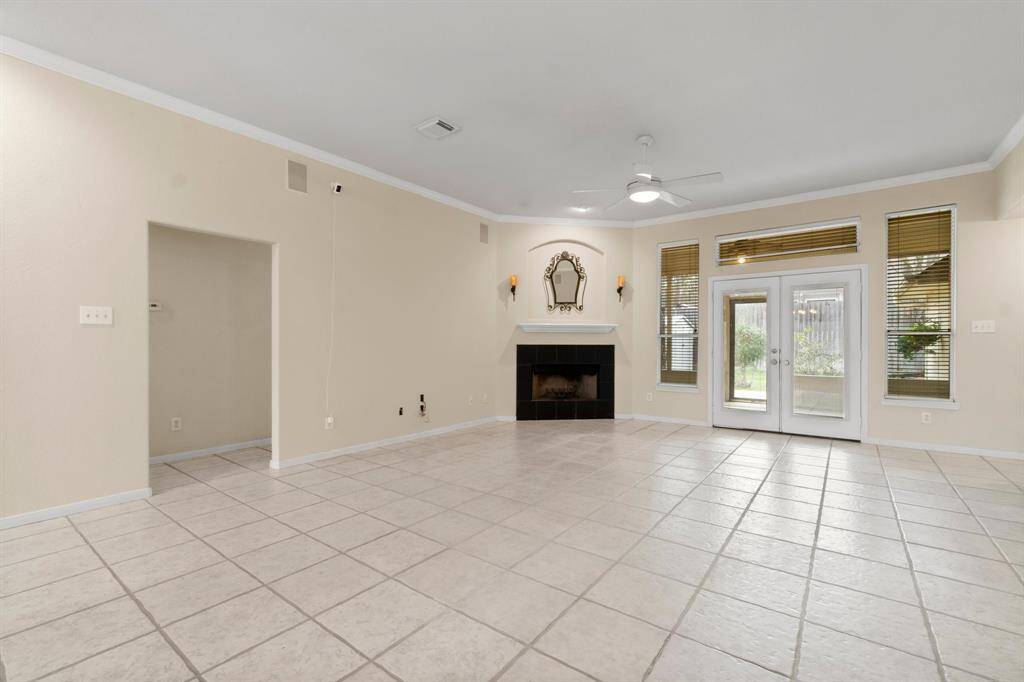 This spacious living area features a tiled floor, a cozy fireplace, and a ceiling fan. It includes a breakfast bar leading to the kitchen and has French doors that open to the outside, offering plenty of natural light.