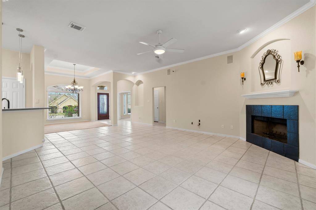 This spacious living room features a tiled floor, a cozy fireplace, and double glass doors leading to the backyard. It has abundant natural light, a ceiling fan, and neutral walls, ideal for personalizing your space.