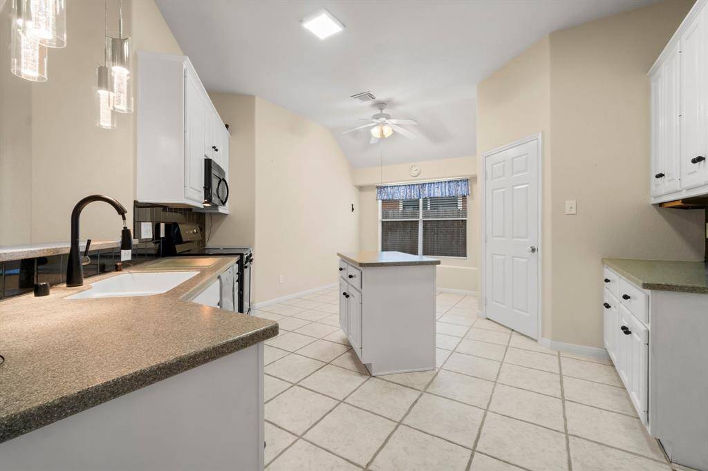 This spacious living area features a cozy fireplace, ceiling fan, and elegant tile flooring. The open layout flows into a dining space with a decorative chandelier. Large windows and glass doors invite natural light, creating a bright and welcoming atmosphere.