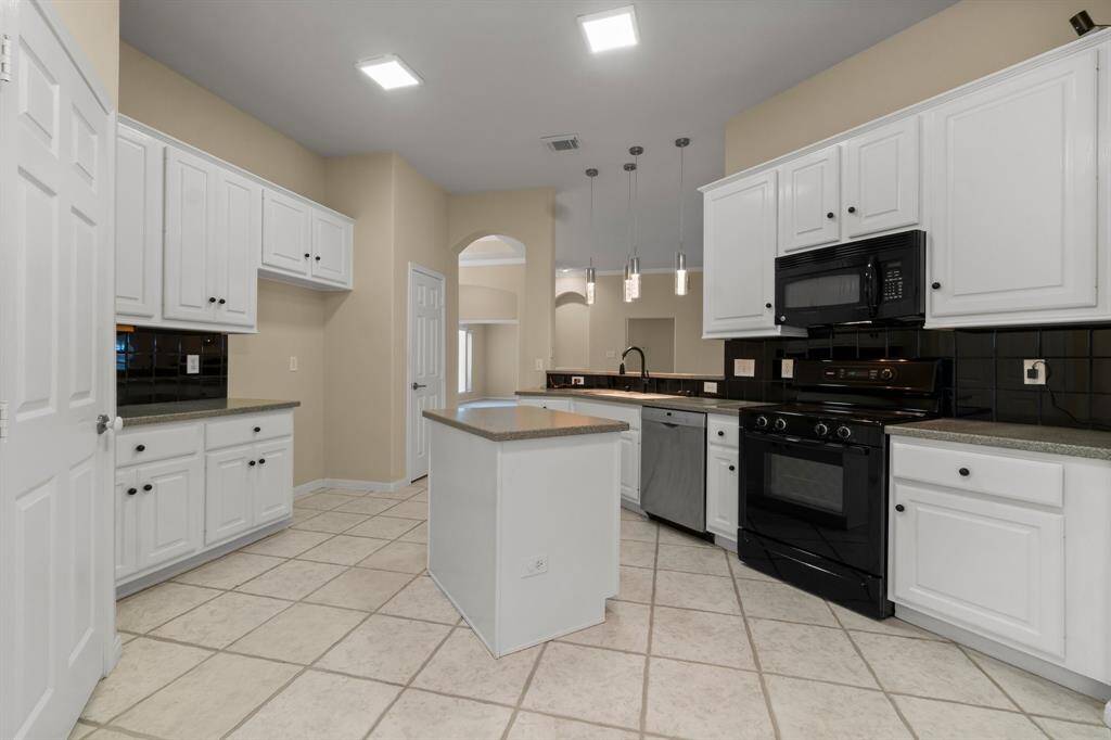 Bright kitchen with modern fixtures, featuring white cabinetry, dark countertops, and a central island. Tile flooring complements the space, which includes a cozy breakfast nook with a ceiling fan and window for natural light.