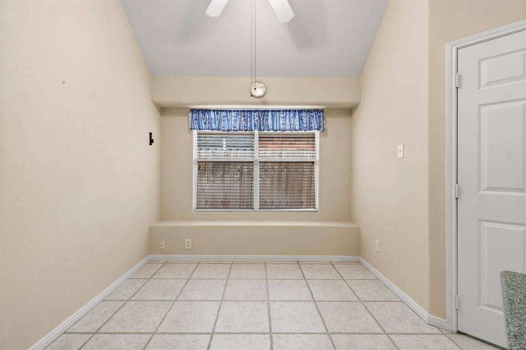 This kitchen features modern appliances, white cabinetry, and black tile backsplash. It offers a spacious layout with ample counter space and a view into a well-lit adjoining room, complemented by stylish pendant lighting.