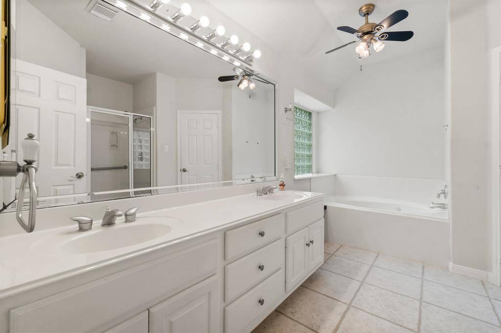 This spacious bedroom features soft yellow walls, a high ceiling with a modern ceiling fan, and plush carpet flooring. It has an en-suite bathroom and large windows for natural light.