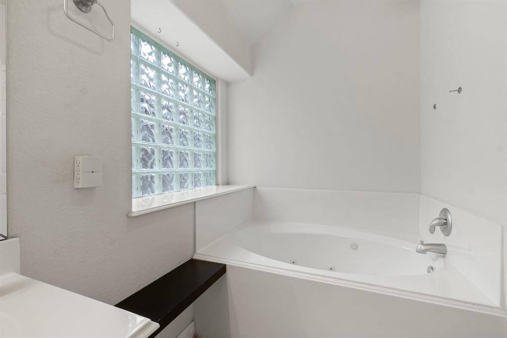 This bright bathroom features a double vanity with ample storage, a large mirror with overhead lighting, a spacious tub, a separate shower, and a ceiling fan for comfort.