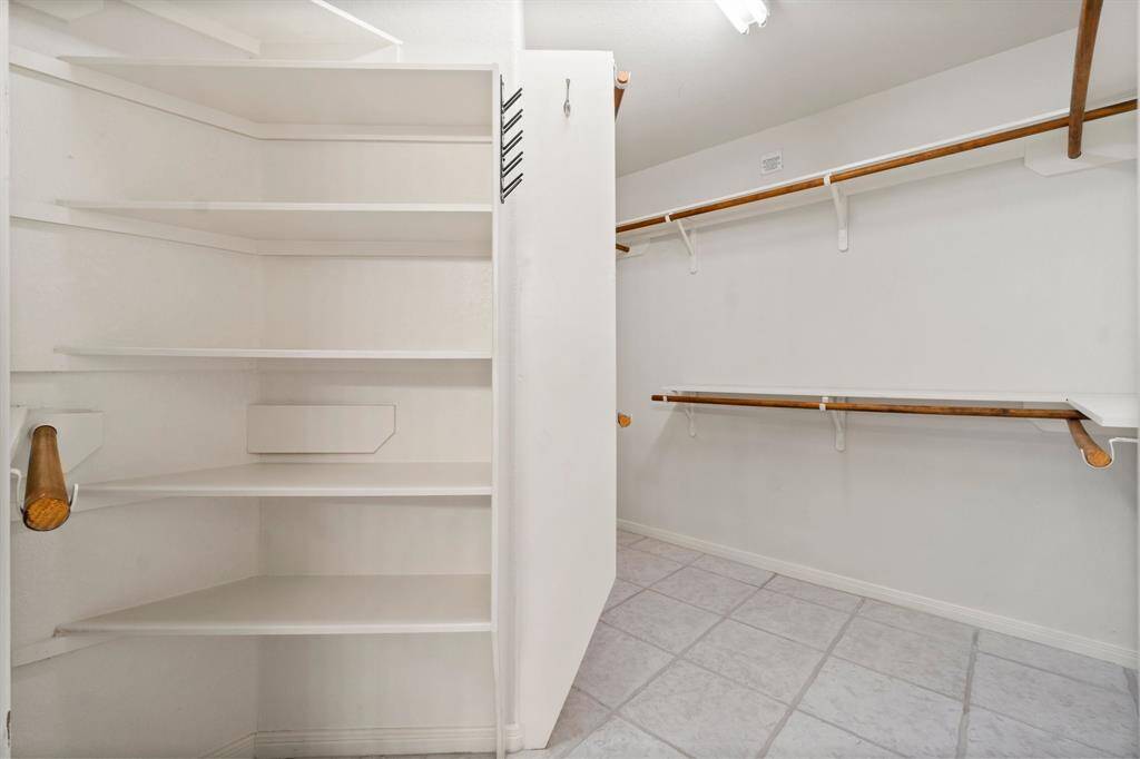 Primary bathroom with a glass-enclosed shower and a door leading to a carpeted Primary bedroom. The bathroom has a tile floor and a vanity with a mirror. The bedroom features a ceiling fan and a large window with drapes.