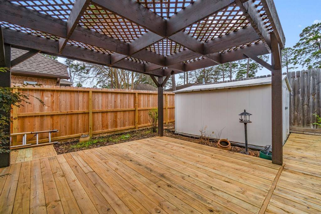 This backyard features a spacious wooden deck with a pergola, perfect for outdoor entertaining. It includes a small lawn area, bordered by a wooden fence, providing privacy and a cozy atmosphere.
