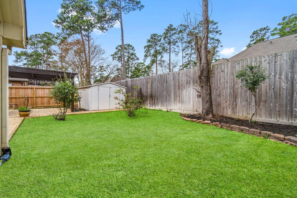 This photo showcases a well-maintained backyard with lush green grass, a wooden deck, and a storage shed. The area is fenced for privacy and features mature trees, providing a serene outdoor space.