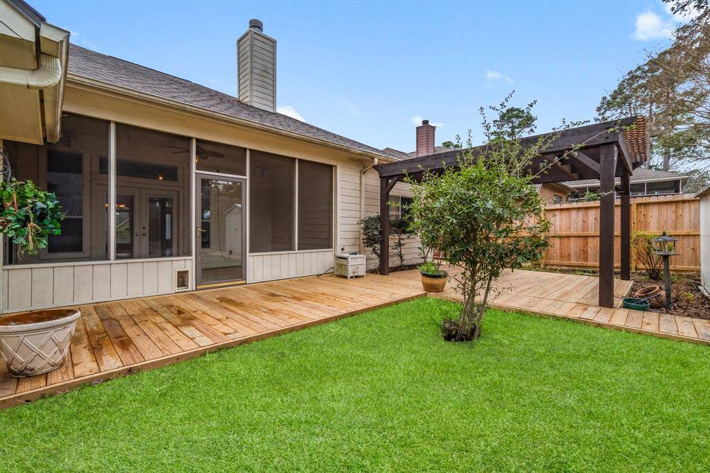 This backyard features a well-maintained lawn, a wooden fence for privacy, and a storage shed. There's a deck area with potted plants, and mature trees provide a natural backdrop.