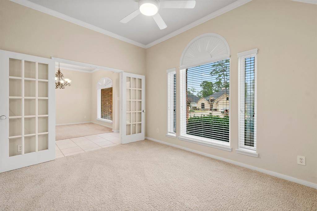 This office room features neutral-walls, carpeted flooring, and a ceiling fan. It has a large window with blinds that let in plenty of natural light, creating a bright and airy atmosphere.