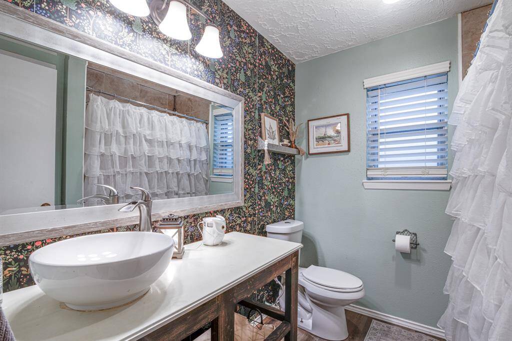 This bathroom features a stylish vessel sink on a rustic vanity with decorative floral wallpaper.