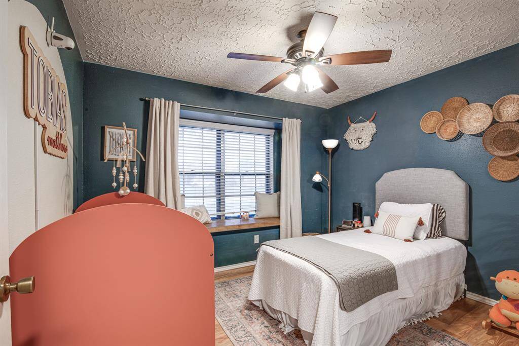 This bedroom features a stylish teal accent wall with a large window seat, perfect for reading or relaxing. The hardwood floor complements the warm, inviting atmosphere.