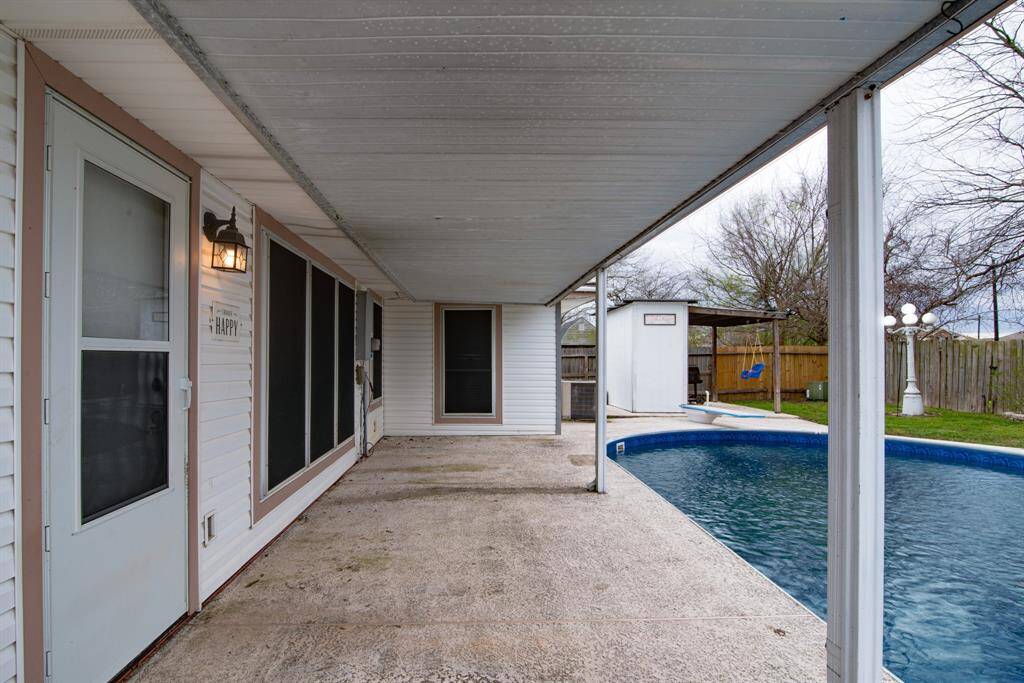 Covered patio leading to a backyard with an in-ground pool. The area is fenced, offering privacy, and features a small shed and green space, ideal for outdoor activities and relaxation.