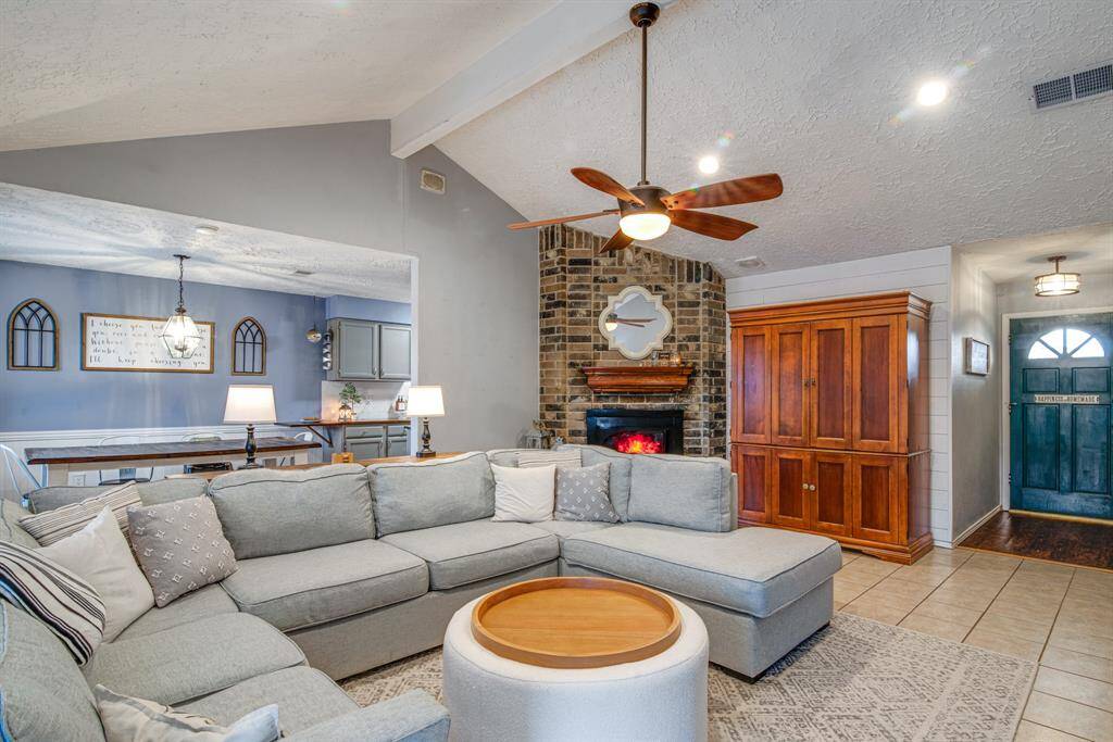 This inviting living room features a cozy corner brick fireplace. The open layout leads to an adjacent dining area with stylish lighting.