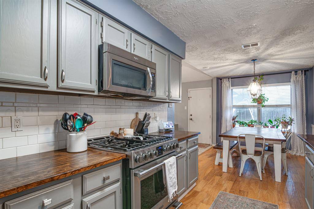 Kitchen and dining area featuring modern gray cabinetry, a sleek stainless steel stove and microwave, and warm wooden countertops. The space is accentuated by a white subway tile backsplash and wood flooring.