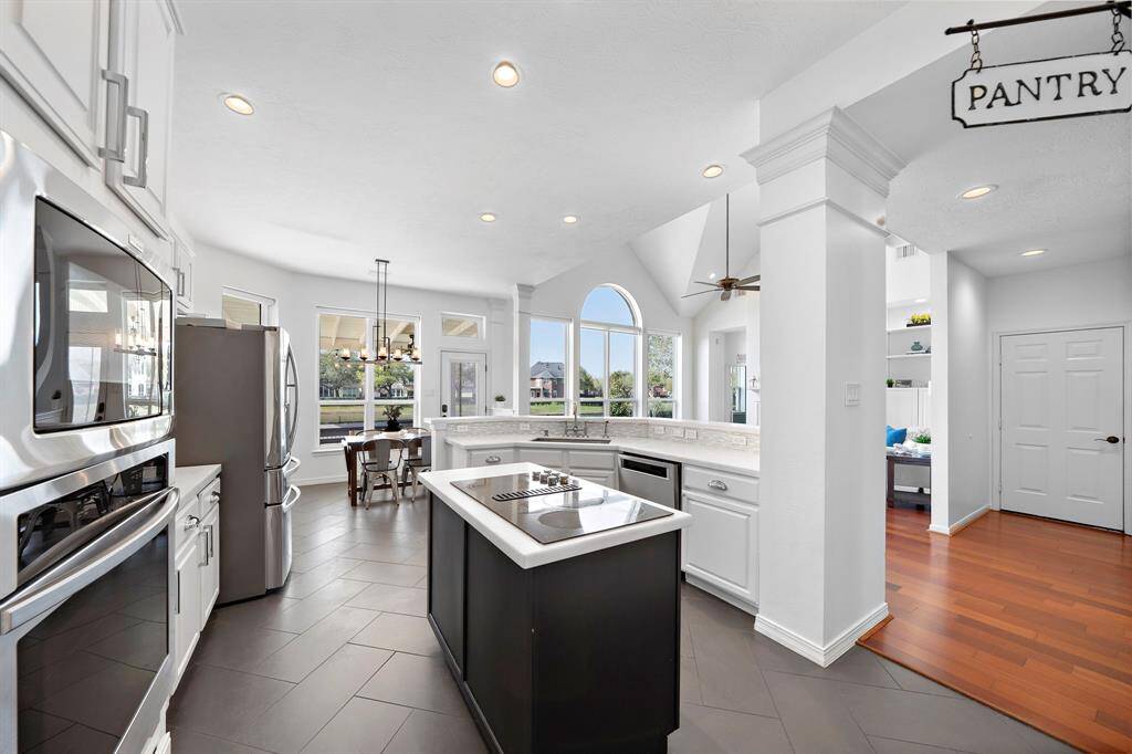 This modern kitchen features sleek stainless steel appliances, a large island with a cooktop, and ample natural light from large windows. The open layout flows into a dining area, creating a bright and inviting space.
