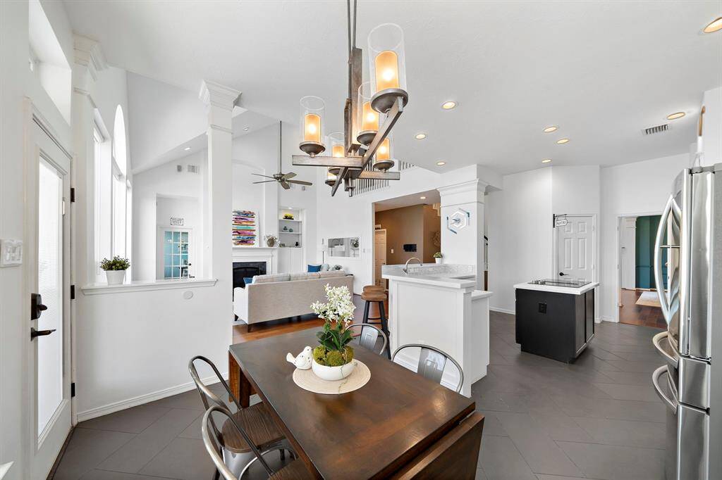 The space features a cozy living area with a fireplace, a stylish chandelier above the breakfast area, and a sleek kitchen with stainless steel appliances.