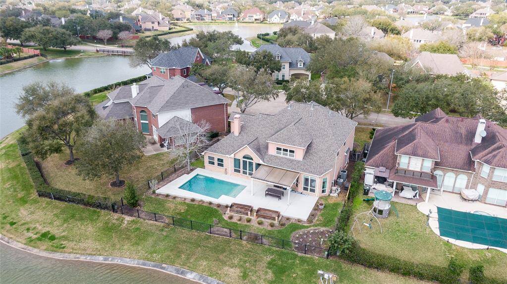 This spacious home features a backyard pool and patio area, situated on a corner lot with a scenic water view. The surrounding neighborhood is lush and well-maintained, offering a tranquil residential setting.