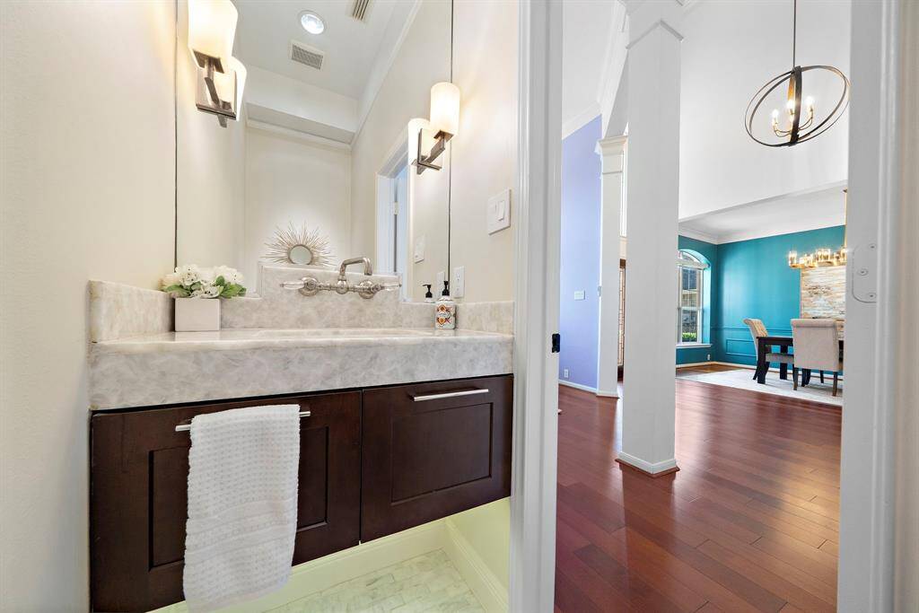 This photo shows a modern powder room with elegant lighting, a stylish vanity, and a marble countertop. Adjacent is a dining area with hardwood floors, vibrant blue walls, and a contemporary light fixture, creating a welcoming and stylish atmosphere.