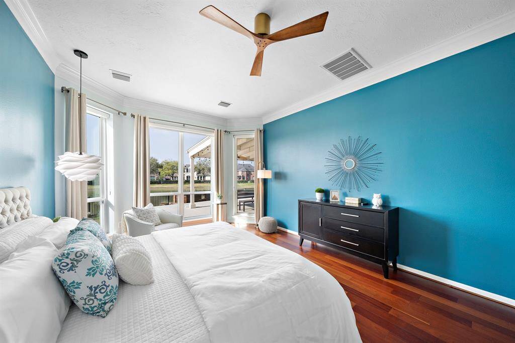 Bright bedroom with a modern design featuring a teal accent wall, hardwood floors, and large windows offering scenic lake views.