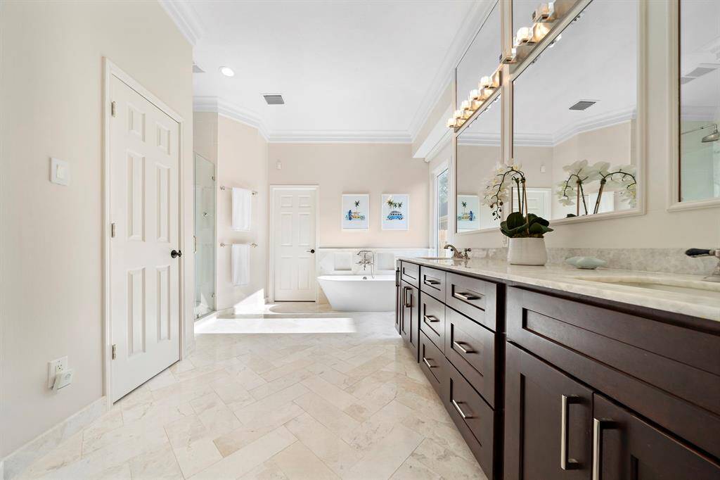 This spacious bathroom features elegant tile flooring, a large double vanity with ample storage, and a soaking tub. Natural light flows in through a window, highlighting the modern fixtures and sleek design.