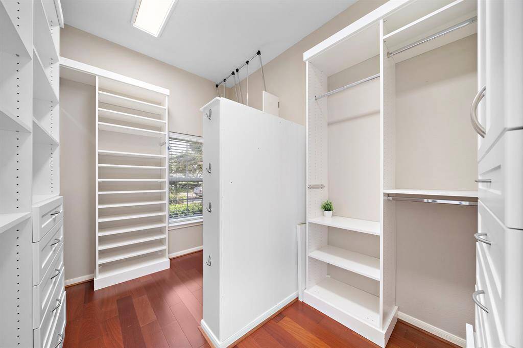 A spacious walk-in closet with hardwood floors and ample built-in shelving and storage units. A large window brings in natural light, making the space bright and functional.