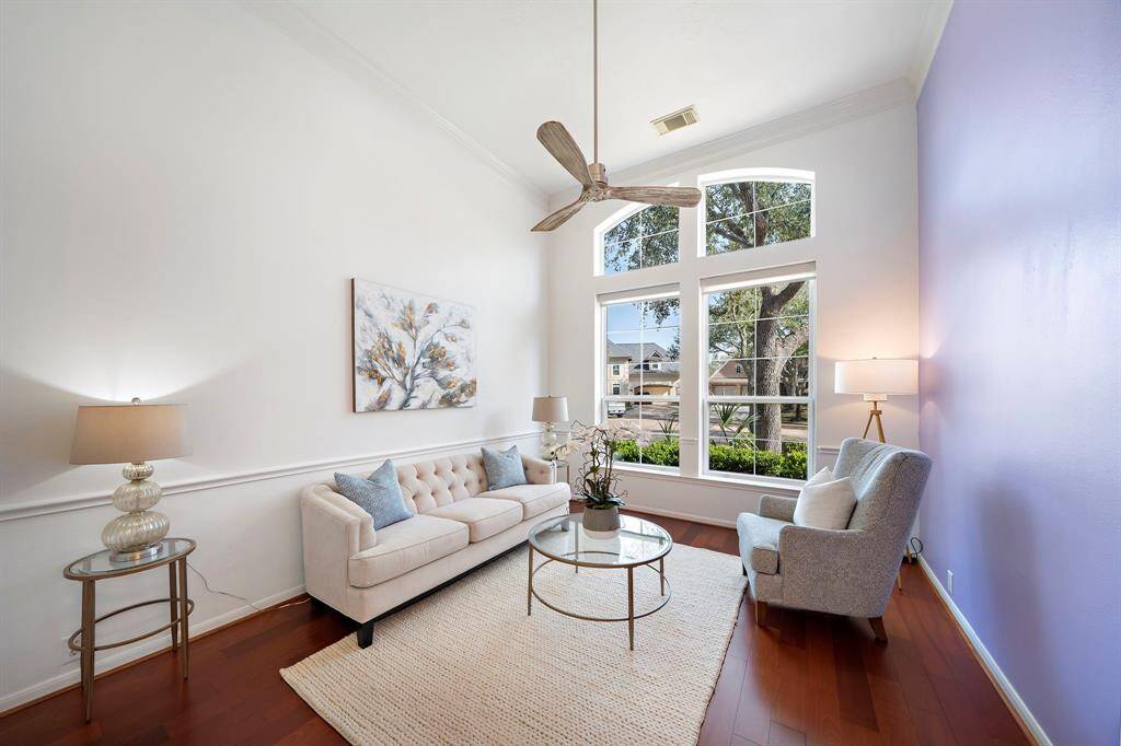 This bright and inviting room features large windows with a view of the street, high ceilings, and a modern ceiling fan.