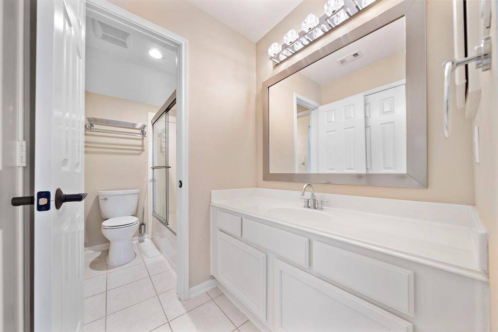 This bathroom features a modern design with a large mirror, ample countertop space, and a clean, bright aesthetic. It includes a shower with glass doors, a toilet, and contemporary lighting.