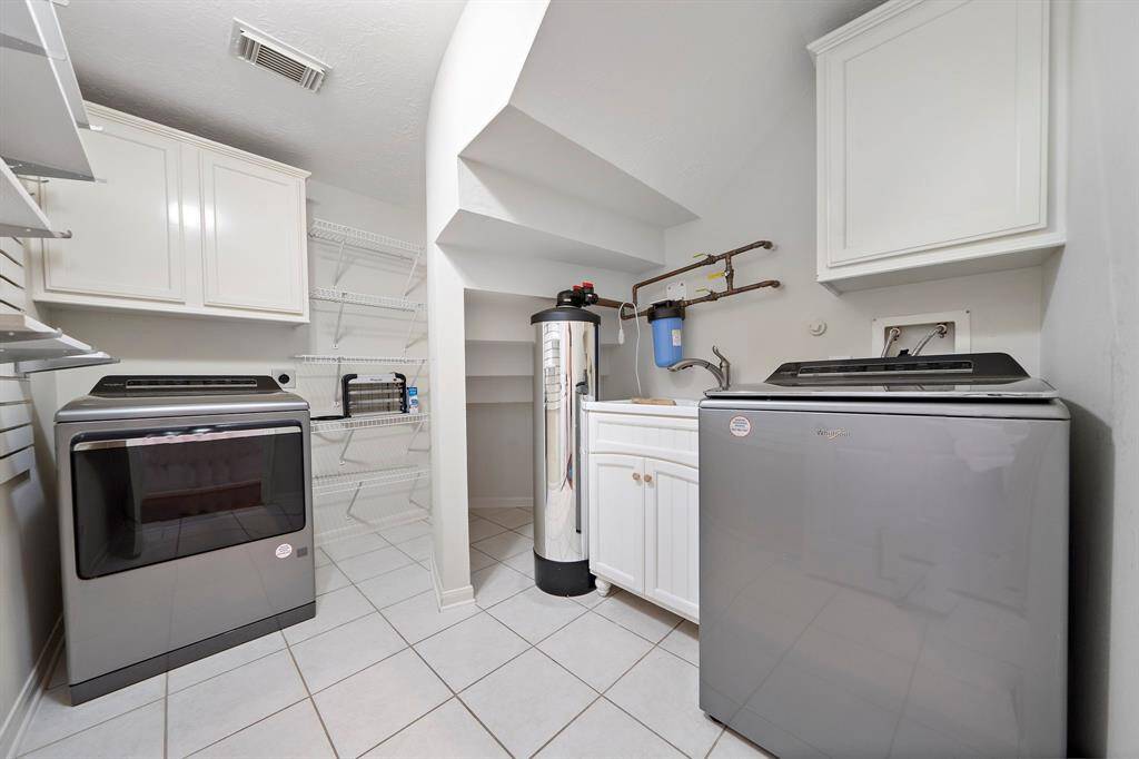 This utility room features modern washer and dryer units, ample cabinet storage, open shelving, and a water filtration system. It offers a clean and efficient space for laundry and storage needs.