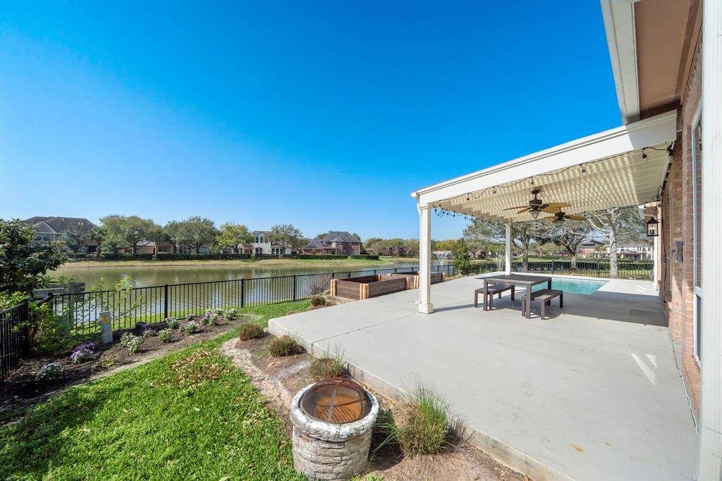 A spacious backyard patio with a covered seating area, overlooking a tranquil lake. The space is perfect for outdoor relaxation and entertaining, with views of neighboring houses across the water.
