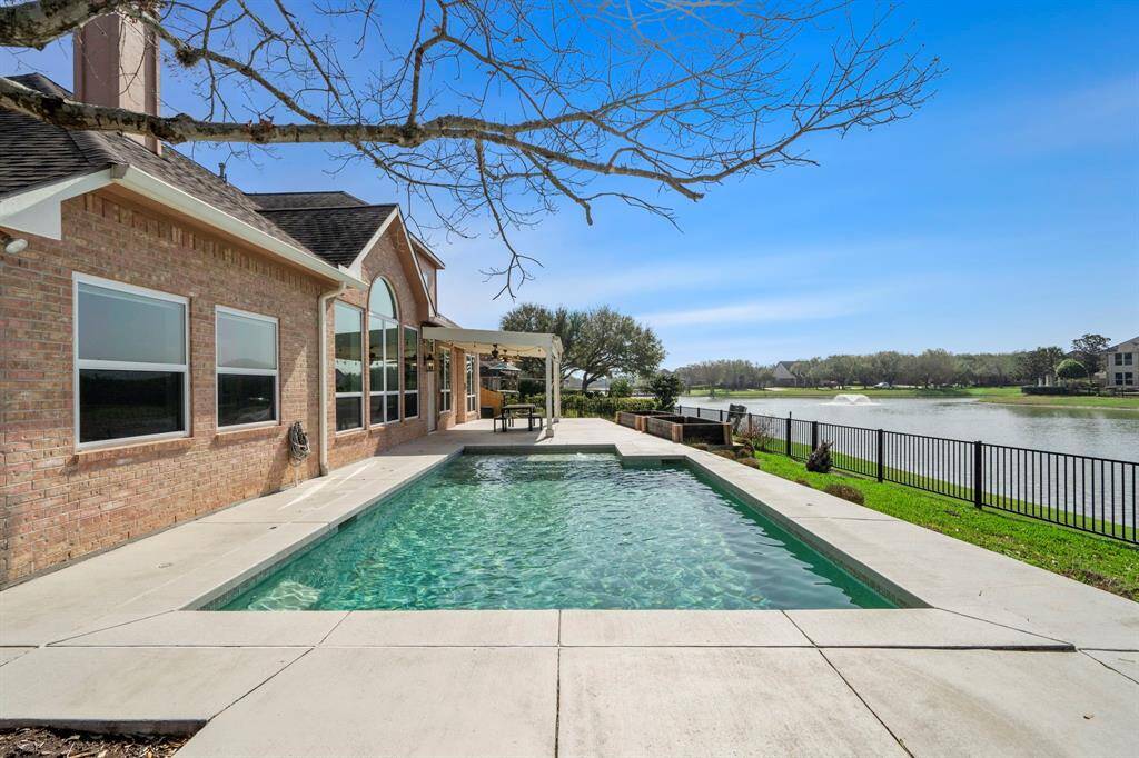 This stunning property features a spacious backyard with a modern pool, overlooking a serene lake. The brick exterior and large windows provide a charming and inviting atmosphere, ideal for relaxation and entertainment.