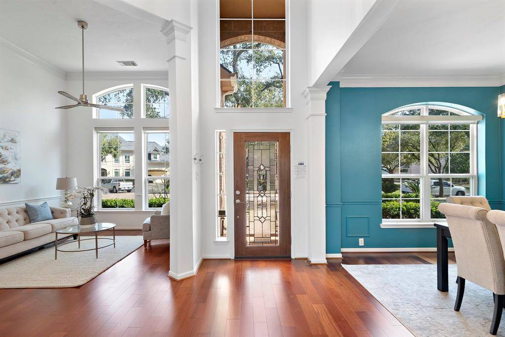 Welcome to a bright, open-entryway with high ceilings and large windows, allowing plenty of natural light. The space features a cherry oak hardwood flooring, a modern ceiling fan, and a stylish mix of neutral and teal walls, creating a welcoming and contemporary atmosphere.