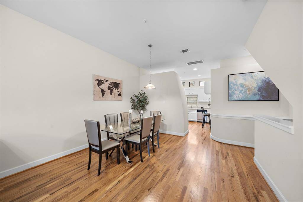 Hardwood floors and a modern glass table with seating for six highlight the dining area. A pendant light fixture illuminates the setting, enhancing the room's inviting elements.