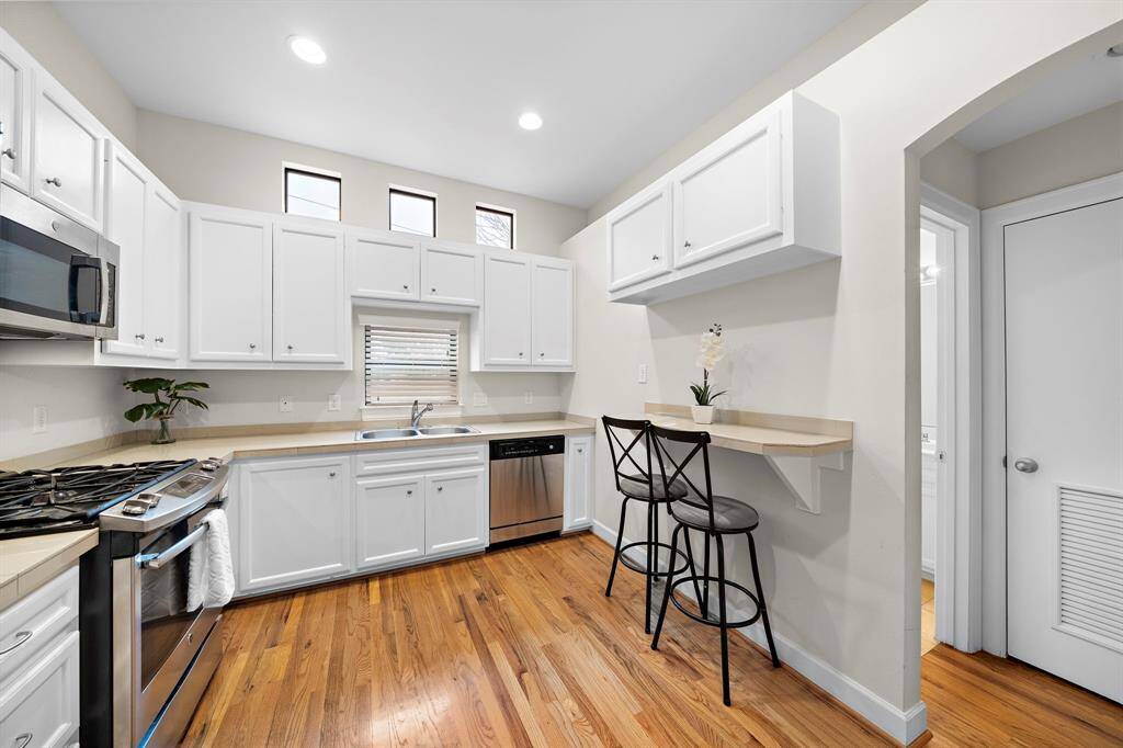 Stainless-steel appliances and bright white cabinets define this kitchen. Wood floors add warmth, while upper windows provide additional sunlight in this efficient space.