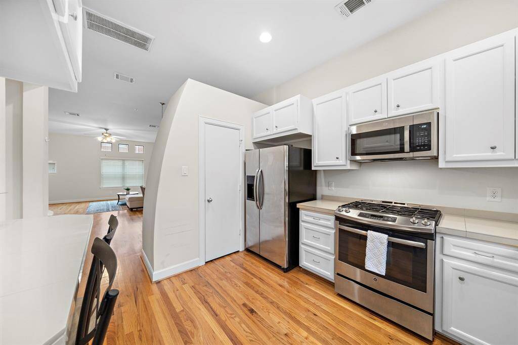 White cabinetry pairs with stainless steel appliances in this modern kitchen space. Gleaming hardwood floors add warmth, while the layout flows into the adjacent living area.