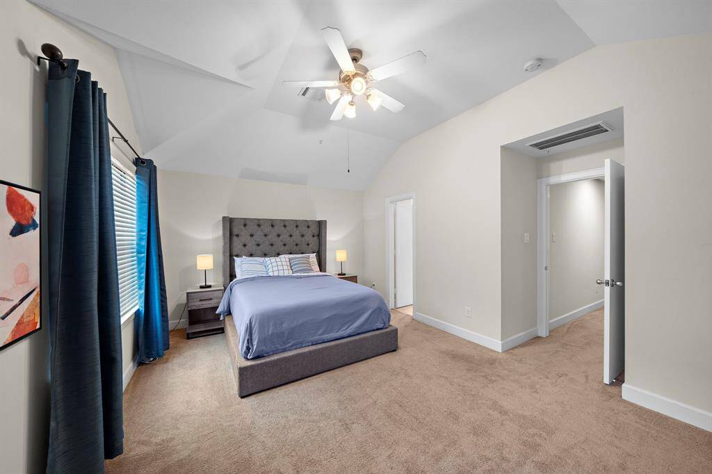 The primary bedroom is spacious and inviting, with plush carpeting and a modern ceiling fan. Vaulted ceilings emphasize its open feel.