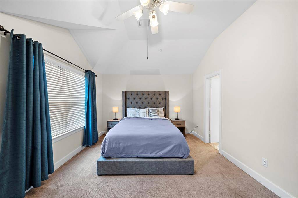 Rest easy in this contemporary bedroom featuring neutral tones, ample natural light, and a ceiling fan. A tufted headboard and streamlined side tables add a sense of refined comfort.