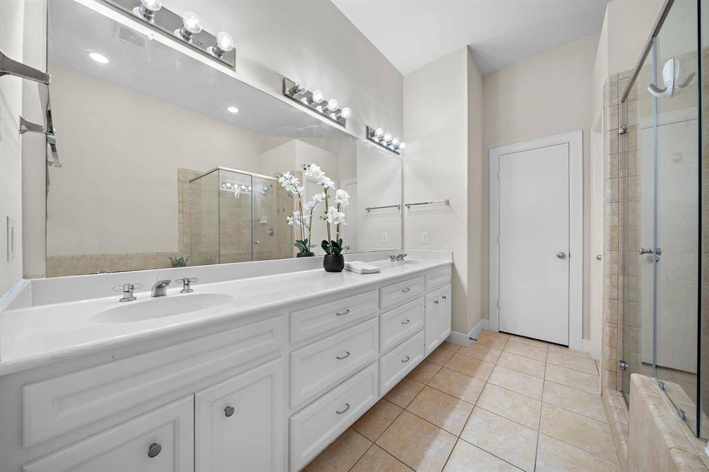 Well-lit primary ensuite bath features a dual-sink vanity with ample storage. A large mirror reflects the space and bright lighting fixtures, ensuring a functional and refreshed space.