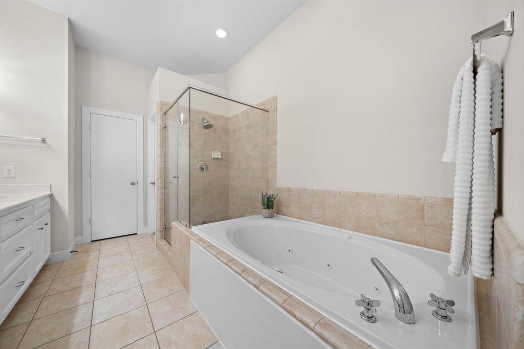 Relax in the jetted soaking tub, situated beneath a tiled shower with glass enclosure. Polished chrome fixtures and neutral tiling create a serene atmosphere in the ensuite bath.