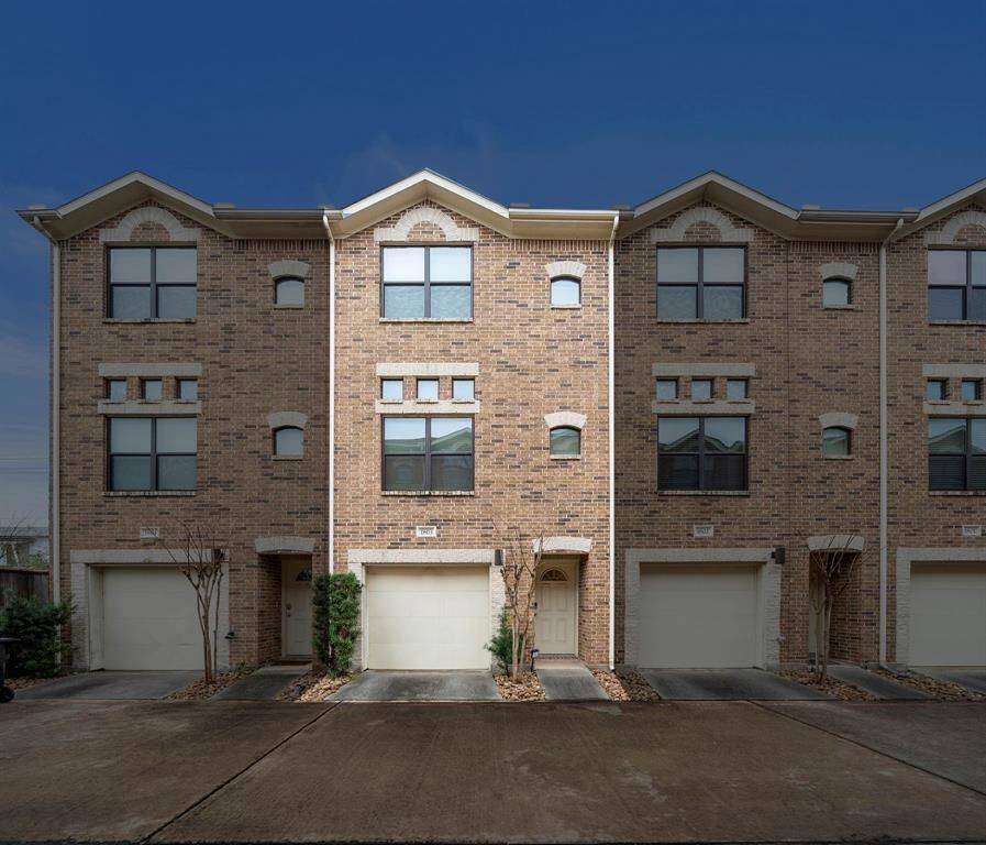 This three-story brick townhome features individual garages for parking and storage. Constructed with subtle brickwork and trimmed windows, the structure is part of a private, gated community.