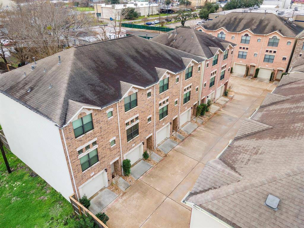 Aerial view highlighting the three-story brick townhome in the gated community. Tandem 2-car garages offer convenience and extra storage plus a lock-and-leave lifestyle. The low maintenance lot and prime location provide easy access to 610.