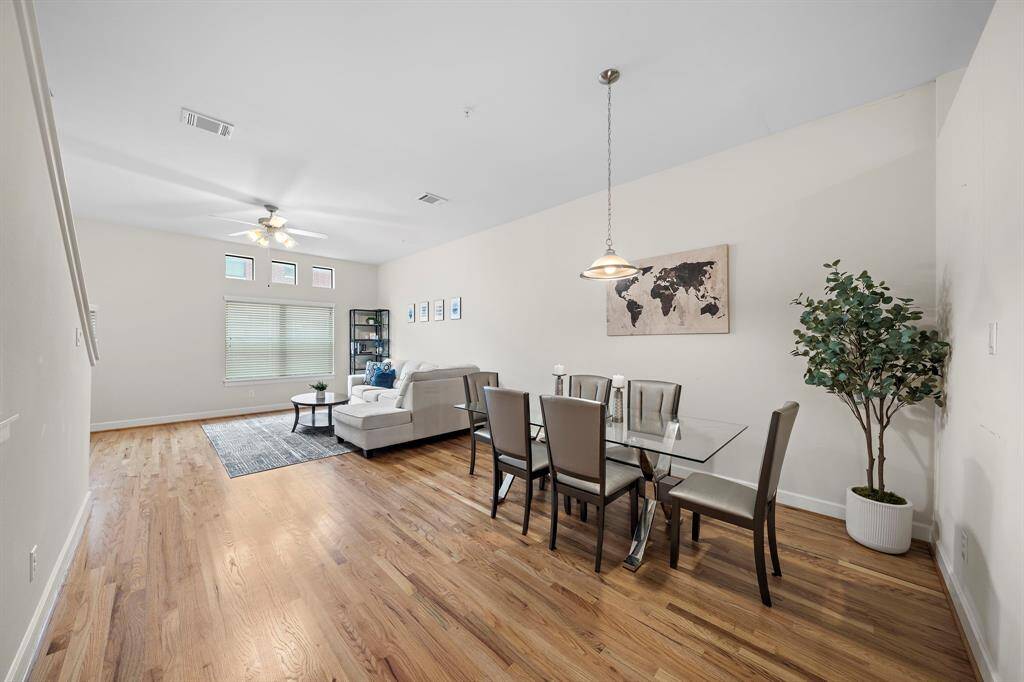 Hardwood floors span this open-concept townhome. Find a dining area with a glass-top table, seating for six and decorative wall art alongside the living area.
