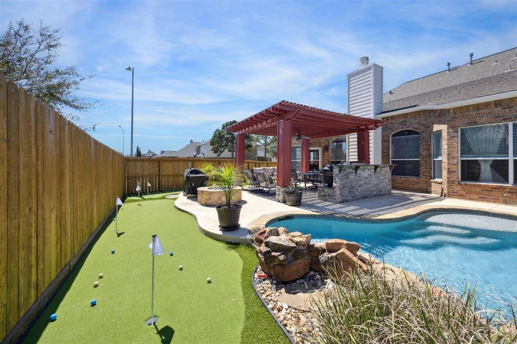 A look back towards the house  Glimmering pool, outdoor kitchen with bar seating on the other side of the Bull and Egg grills.  More turf ahead and to the left.  The fence was recently stained.