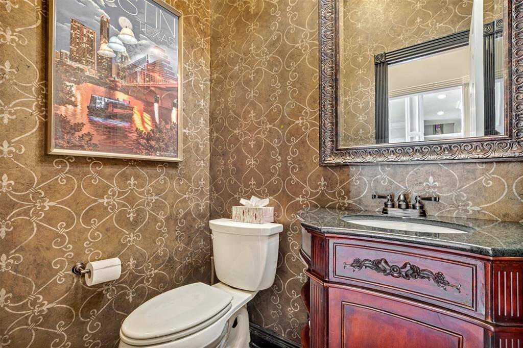 The stylish powder room has elegant wallpaper, a wood vanity cabinet with a dark countertop, and ornate mirror.