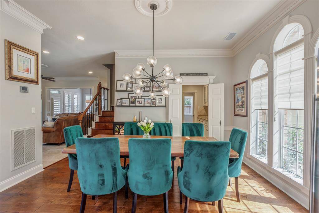 The dining area is bright and open with large windows featuring plantation shutters and fun modern pendant light. The room has wood flooring and a neutral color scheme, providing a inviting atmosphere.