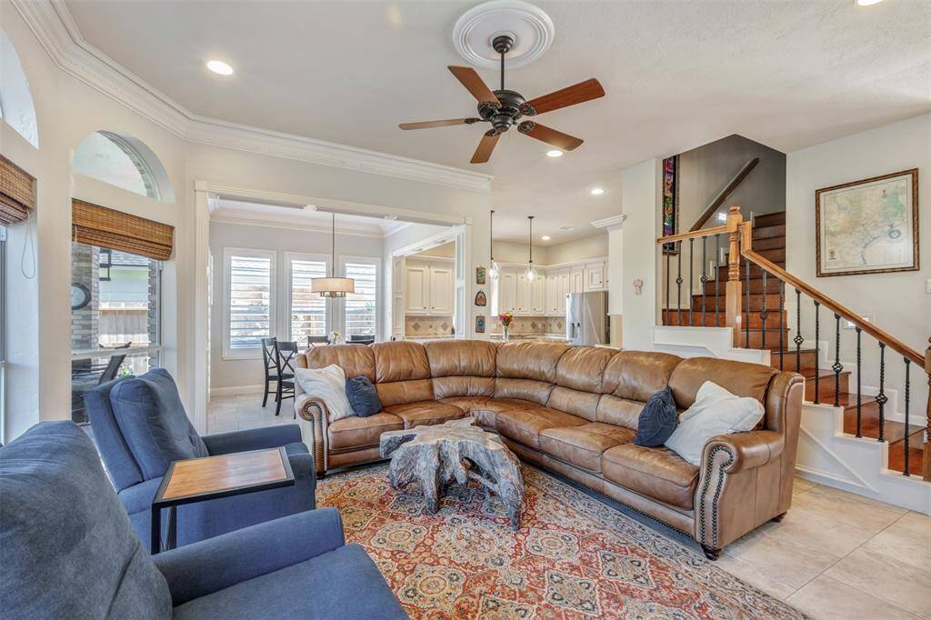 The inviting family room features an open layout flowing into a bright breakfast nook and modern kitchen. The room is accented by a ceiling fan, recessed lighting, and staircase with wood and iron accents. Large windows and neutral tones create a cozy, spacious atmosphere.