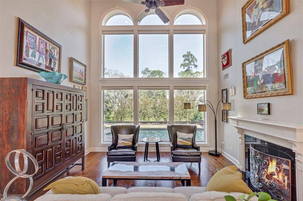 The spacious living room features a high ceiling with large arched windows, offering plenty of natural light and scenic views. It includes a cozy fireplace and elegant moldings, creating a warm and inviting atmosphere.
