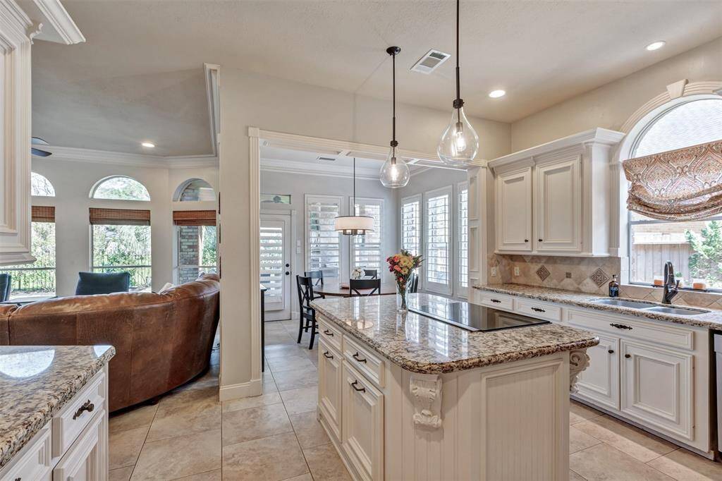 The kitchen showcases a bright, open space with granite countertops, white cabinetry, and modern pendant lighting. It flows seamlessly into the family room with a view of the outdoors and an adjacent breakfast nook featuring large windows with plantation shutters.