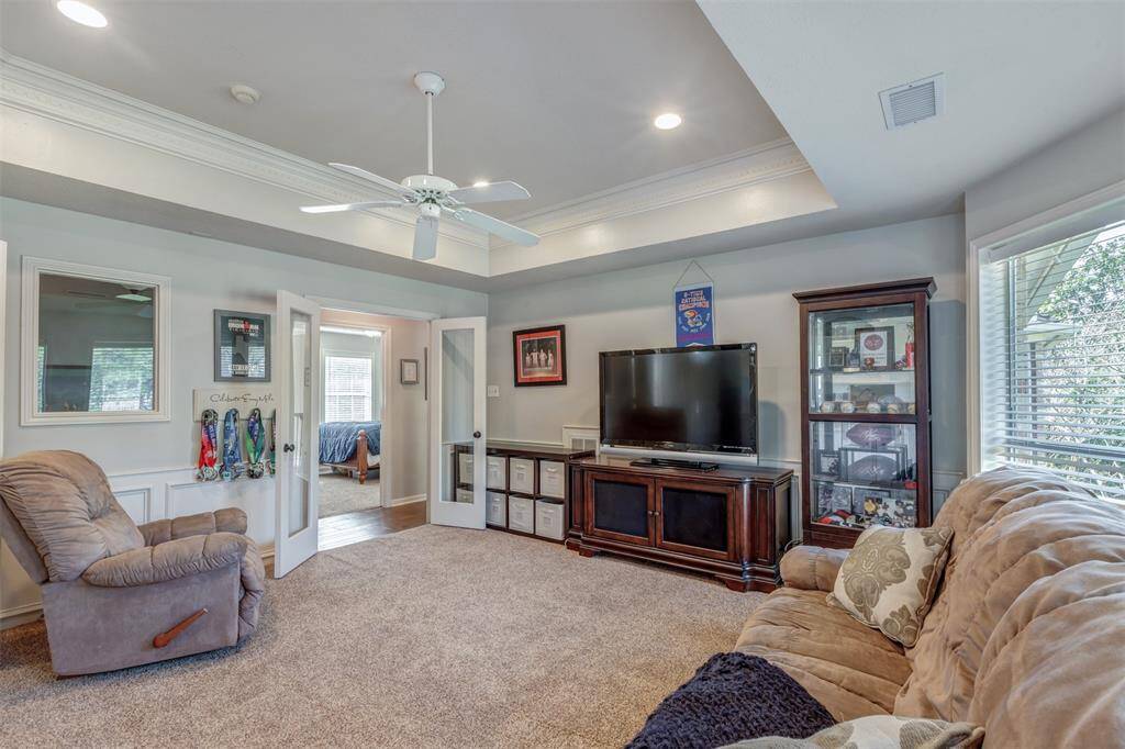 The upstairs game room has plush carpeting, a ceiling fan, and ample natural light from large windows. It includes built-in cabinetry for storage. The room can be closed off with French doors, if desired.