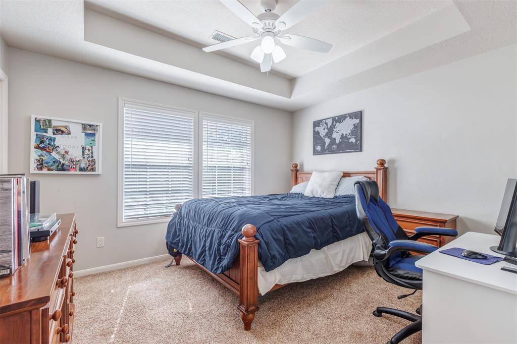 One of the spacious secondary bedrooms overlooks the front yard. The room has a ceiling fan, large windows with blinds, neutral color walls, and a large closet.