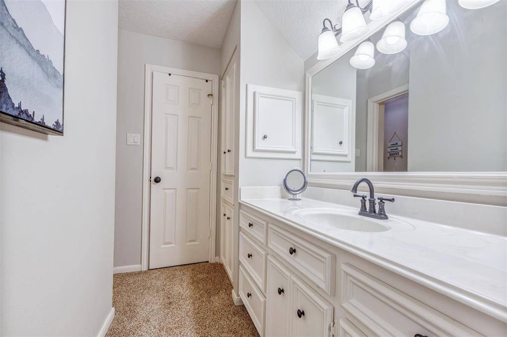 This bathroom features a spacious vanity with elegant fixtures and ample storage, just beyond the closet door is a door to huge walk in attic storage/ known fondly as a "Texas basement." The large mirror and soft lighting enhance the room's brightness.