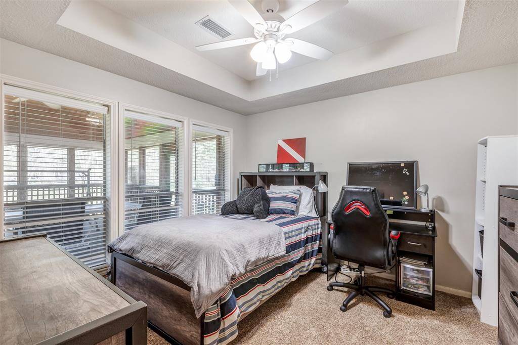Another secondary bedroom overlooks the outdoor living area with natural light from large windows with blinds. The room has carpet, tray ceiling and a ceiling fan, creating a comfortable and functional space.